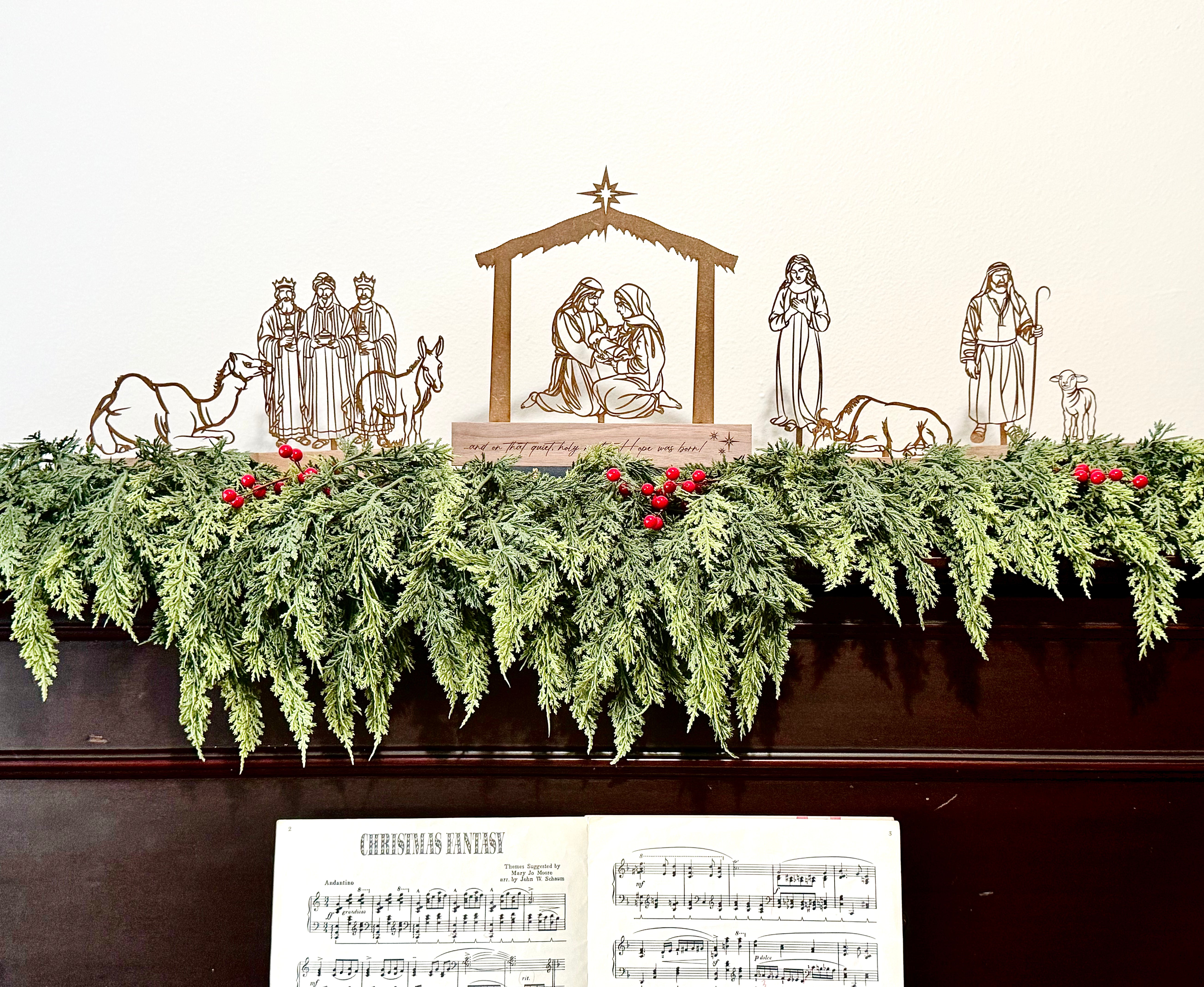 Decorative Christmas display with nativity scene, garland, and sheet music on top of a piano.