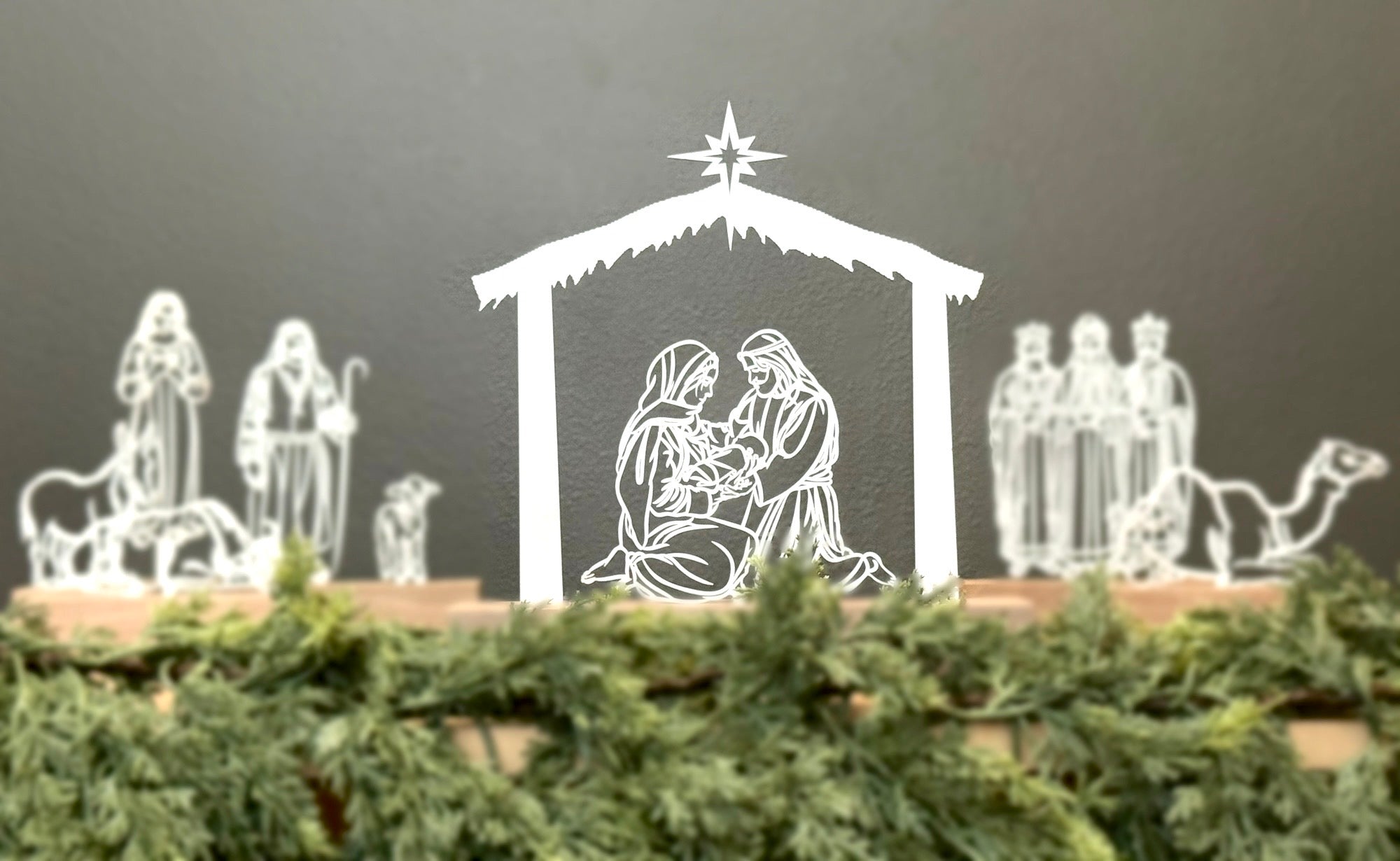 White nativity scene figures on a dark background with greenery at the base.