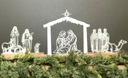 White nativity scene figures on a dark background with greenery at the base.