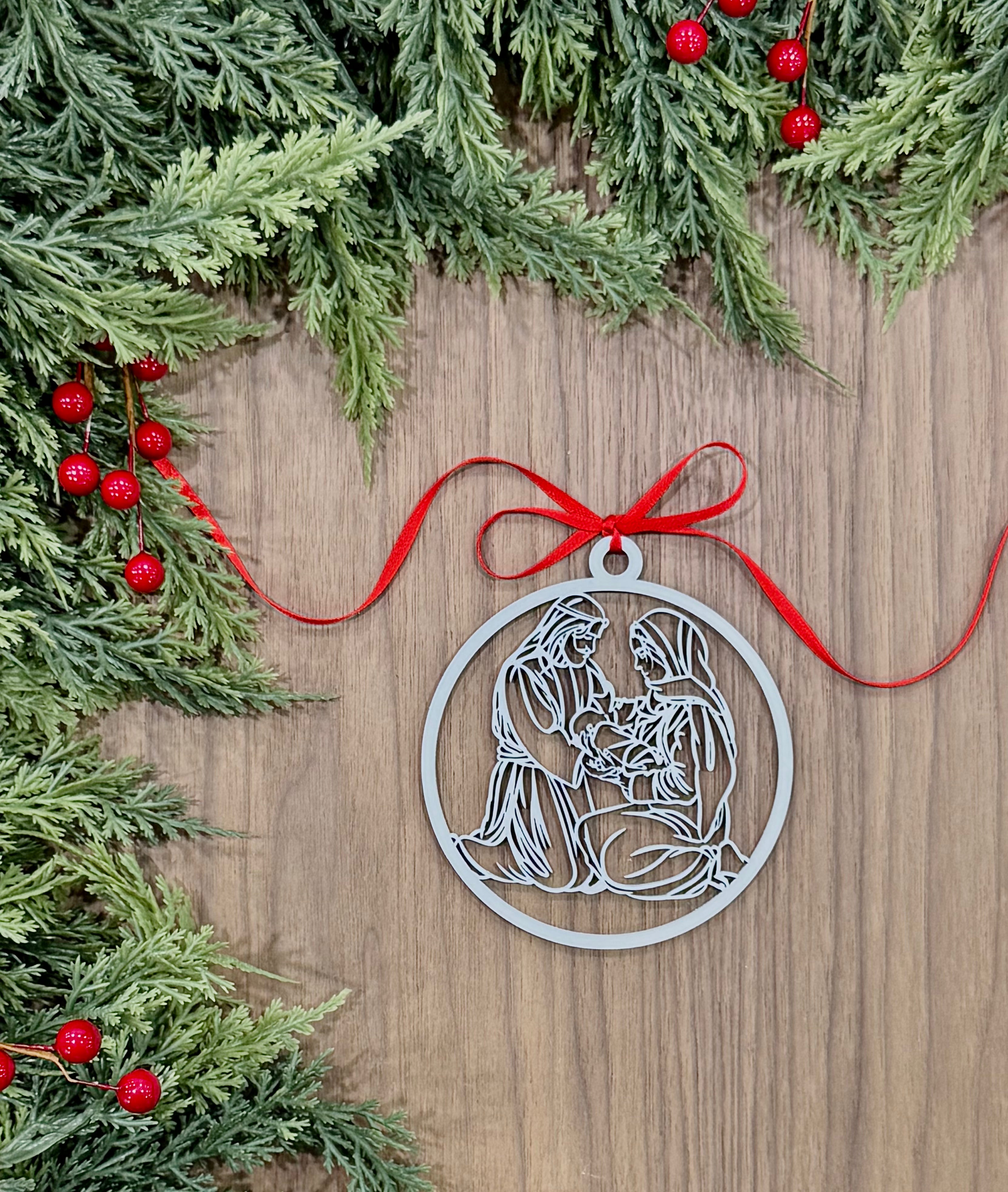 Silver nativity scene ornament on a wooden surface with Christmas greenery and red berries.