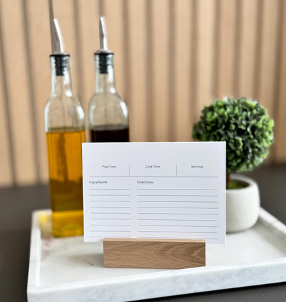 White recipe card on a wooden stand with bottles and a plant in the background