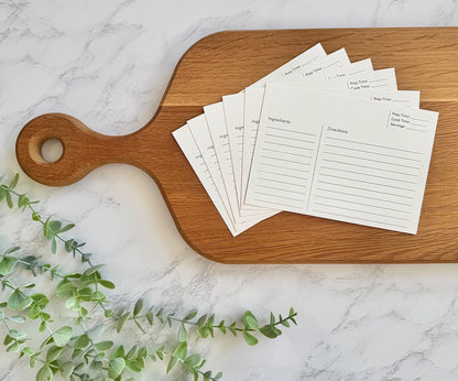 Set of recipe cards on a wooden cutting board with greenery on a marble surface