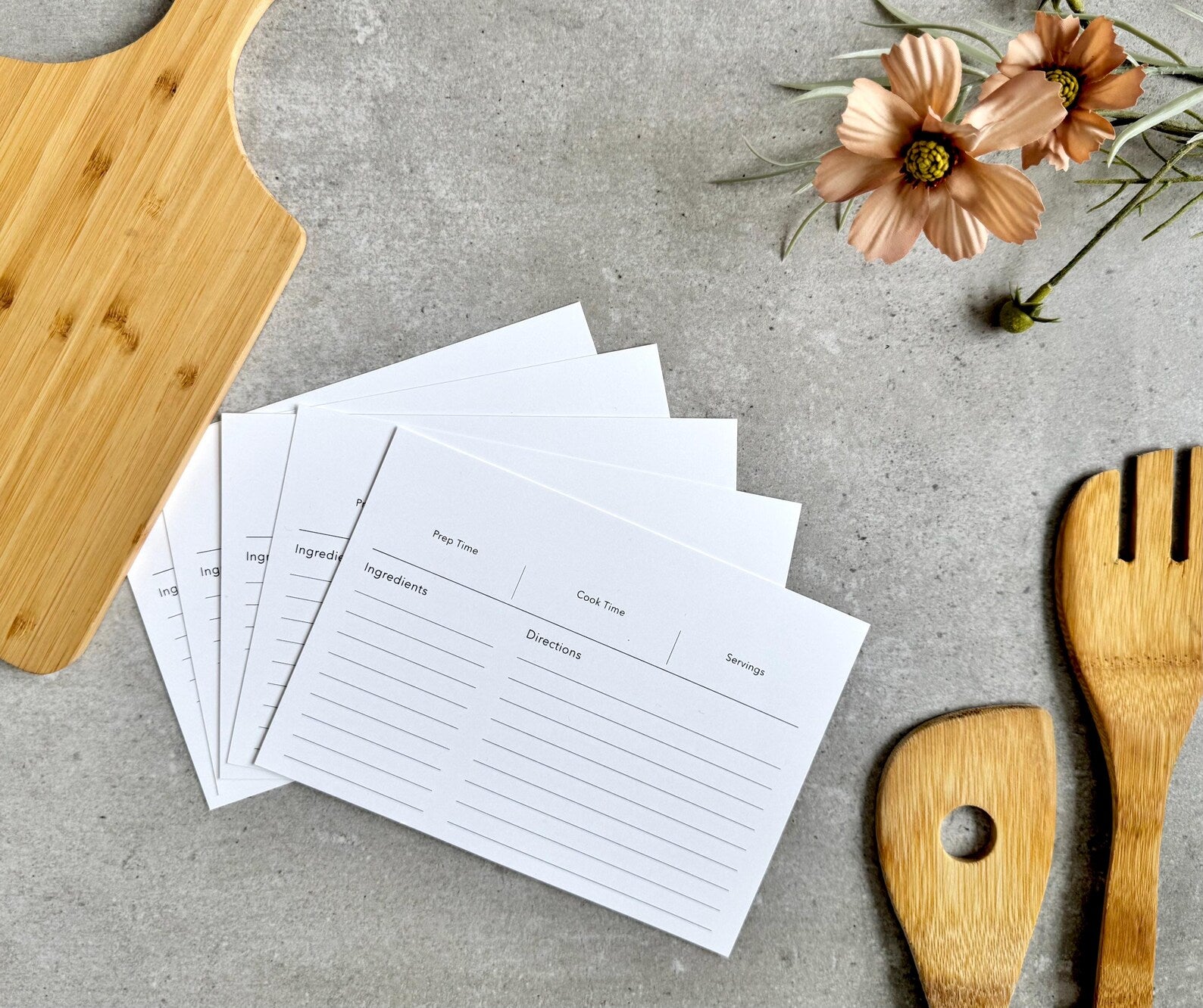 Set of recipe cards on a gray surface with wooden utensils and flowers.