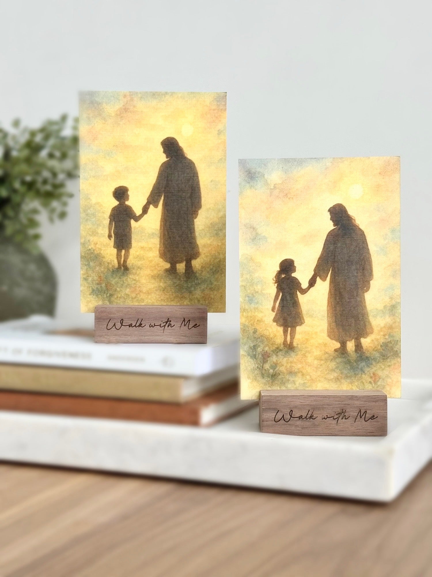 Two prints in stands with silhouettes of a Jesus and child holding hands, set on a white surface.